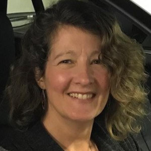 White woman with curly brown hair smiling at the camera 