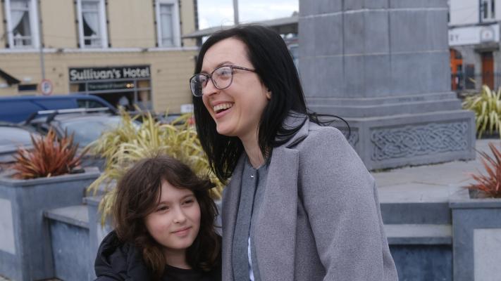 A dark haired woman in glasses and a pale grey coat (Iryna) with a young girl in a black hooded jacket (her daughter) in Market Square, Gort, Co. Galway. 